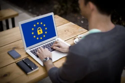 Un homme seul travaille à son ordinateur, illustrant le chef d'une TPE ou micro-entreprise. Un cadenas entouré des étoiles de l'Union européenne évoque la conformité attendue au RGPD.