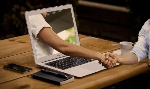 Une main sort de l'écran et serre celle d'une personne assise devant l'ordinateur. Illustrant le partenariat entre DPO interne à l'entreprise et le DPO qualifié de Conformity Data