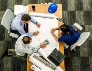 3 personnes assises à une table de travail examinent l'avancement d'un projet. La prise de décision s'appuie sur une réflexion collégiale